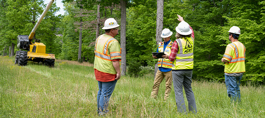 A safety audit program is represented by a group of workers all wearing high-vis vests and white hardhats in an outdoor setting.