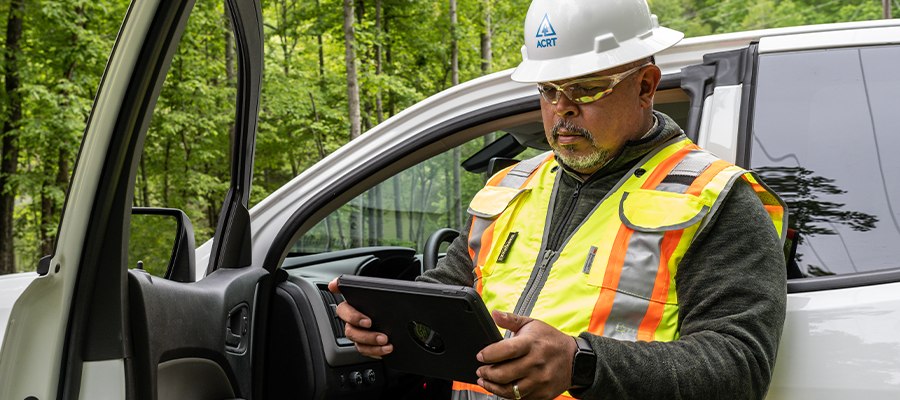 A professional wearing a high-vis vest and white hardhat, holding a tablet represents using technology for proactive fire prevention.