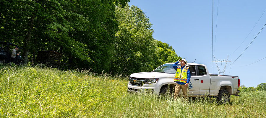 A utility forester wearing a high-vis vest stands in a ROW while work auditing.