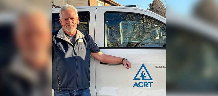 A man wearing a navy ACRT vest stands beside a white truck with the ACRT logo on the door, resting his arm on the open window.